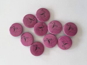 Das Bild zeigt pinkfarbene Ansteckbuttons mit fliegender Biene.