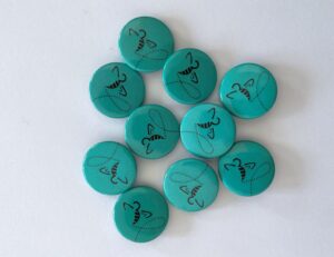 Das Bild zeigt türkisfarbene Ansteckbuttons mit fliegender Biene.